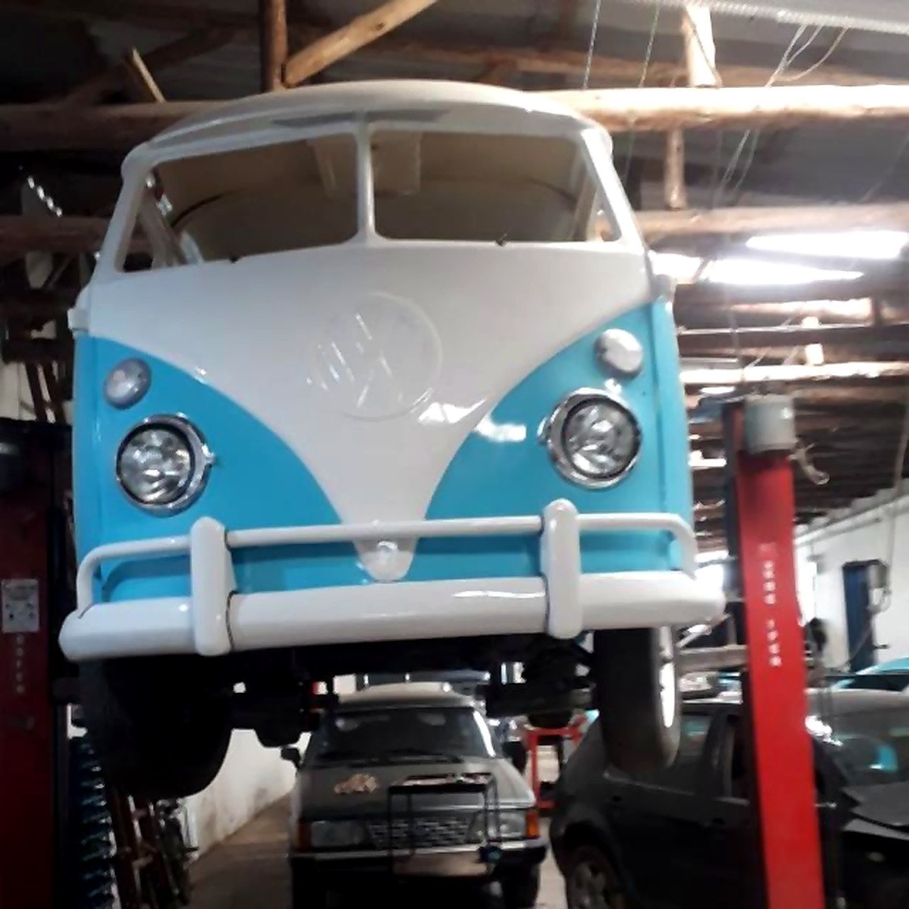 Kombi clássica azul e branca suspensa no elevador da oficina